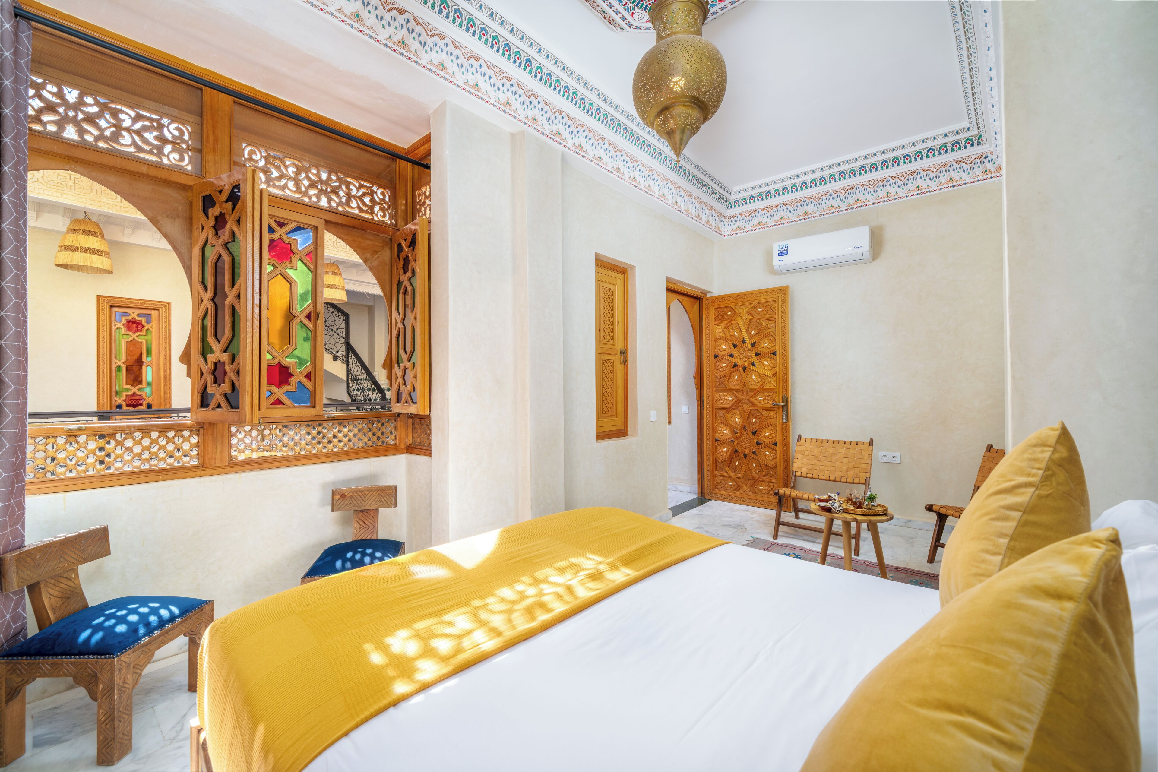 Habitación de hotel con cama, muebles de madera, techo decorativo y una pequeña mesa con una silla.