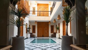 A spacious indoor pool area with a tiled floor, surrounded by large potted plants and a wooden door with intricate carvings. - Riad Nadalinn (Marrakech)