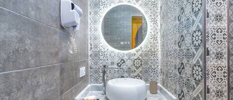 A bathroom with patterned tiles, a sink, a mirror, and towels.