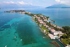An aerial view of a coastal town with a marina, buildings along the waterfront, and clear blue waters. - Hotel Tre Vele (Sirmione)