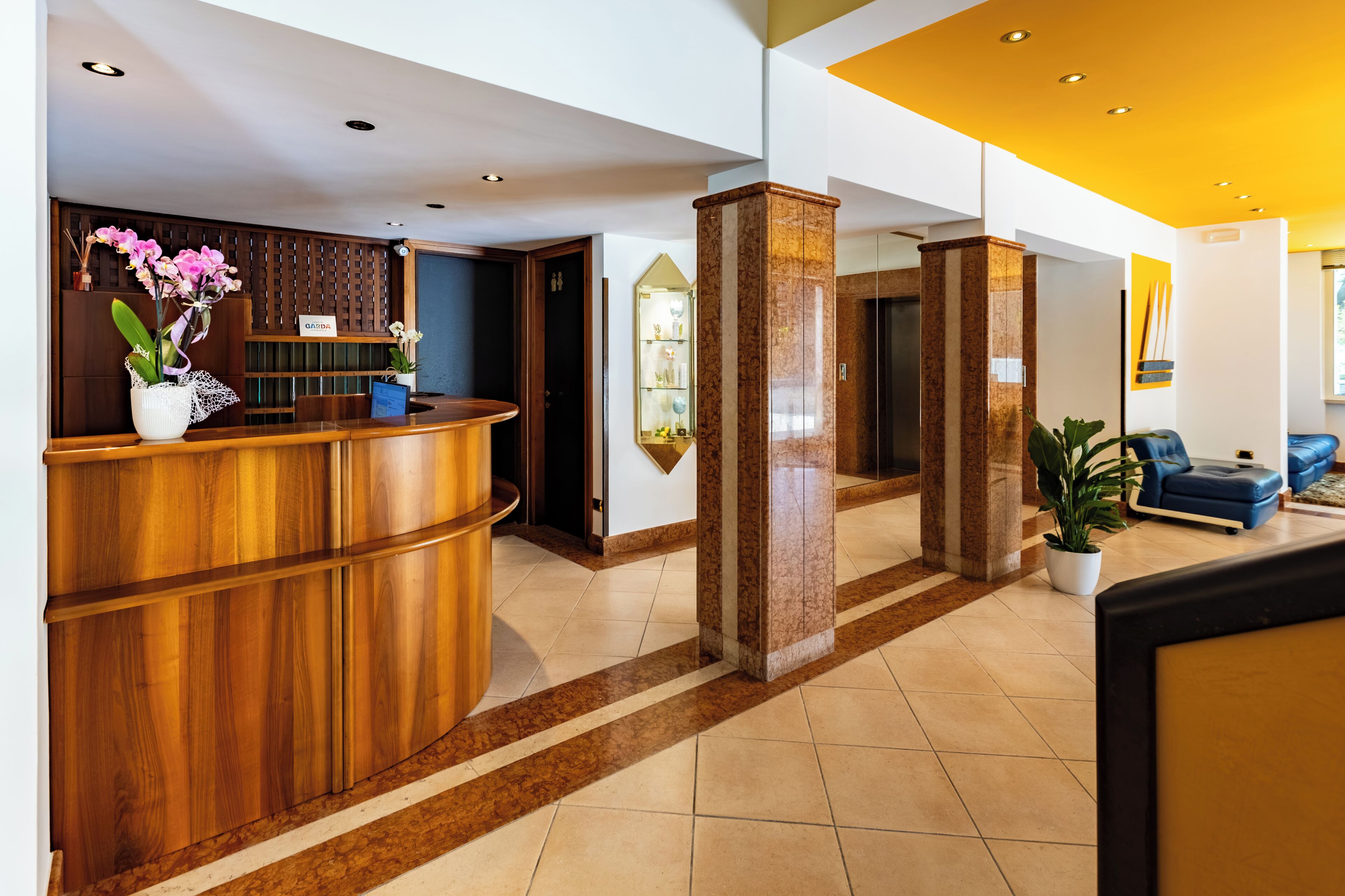 Un espace d’accueil d’hôtel avec un comptoir de réception en bois, une plante en pot et un canapé bleu.