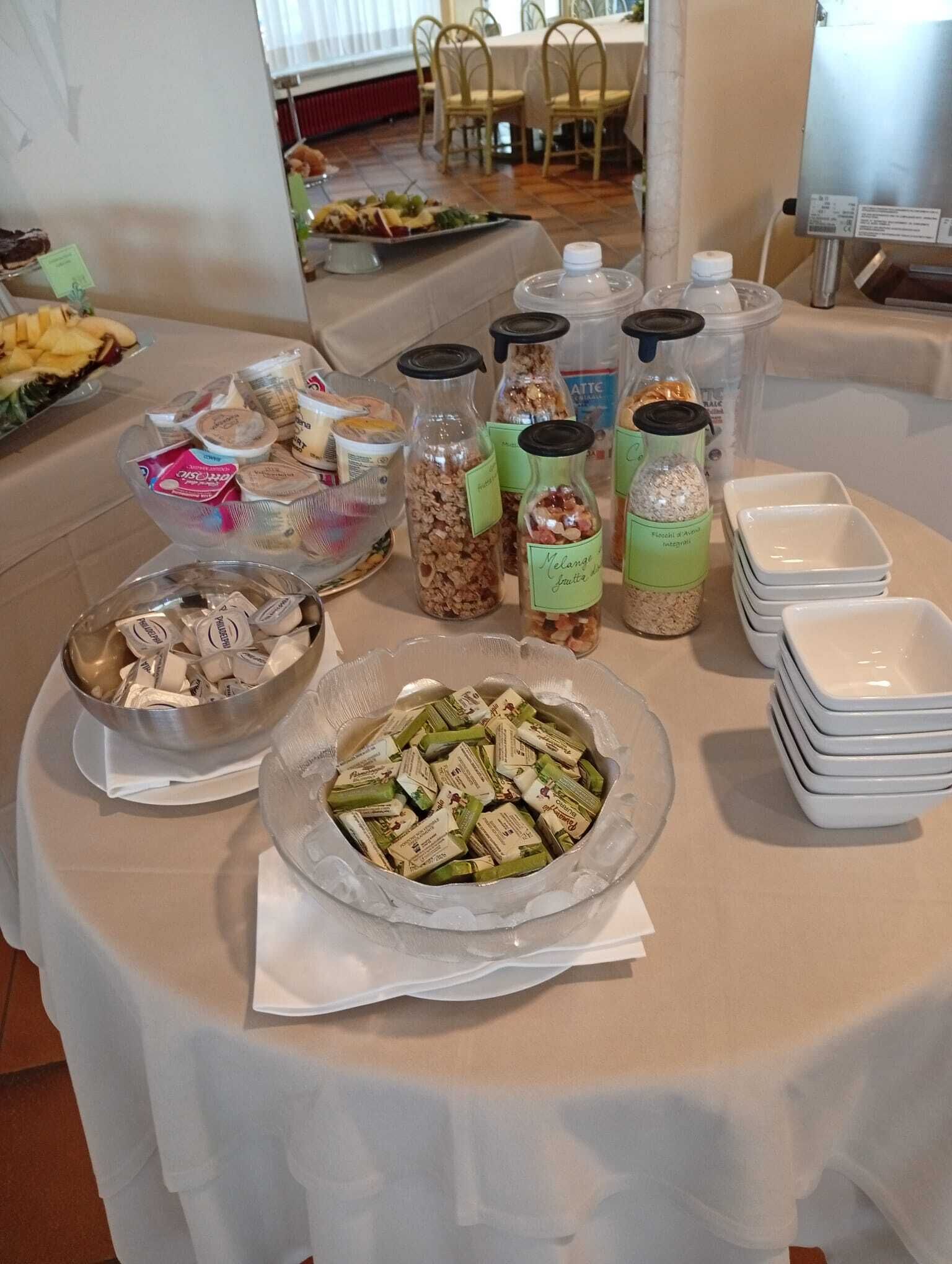 Una mesa de buffet con diferentes opciones de comida, incluyendo un bol de verduras, frascos de salsas y pilas de platos blancos.