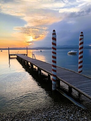 Eine Holzsteg, der sich in ruhiges Wasser erstreckt, mit einem Sonnenuntergang im Hintergrund.