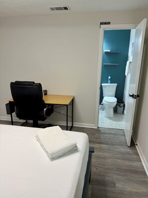 A hotel room with a bed, a desk, a chair, a bathroom with a toilet and sink, and a door leading to the bathroom. - Secret Garden - Self Check-in - 1 bd, 1bath Elegant Apt/Studio (Orange Park)