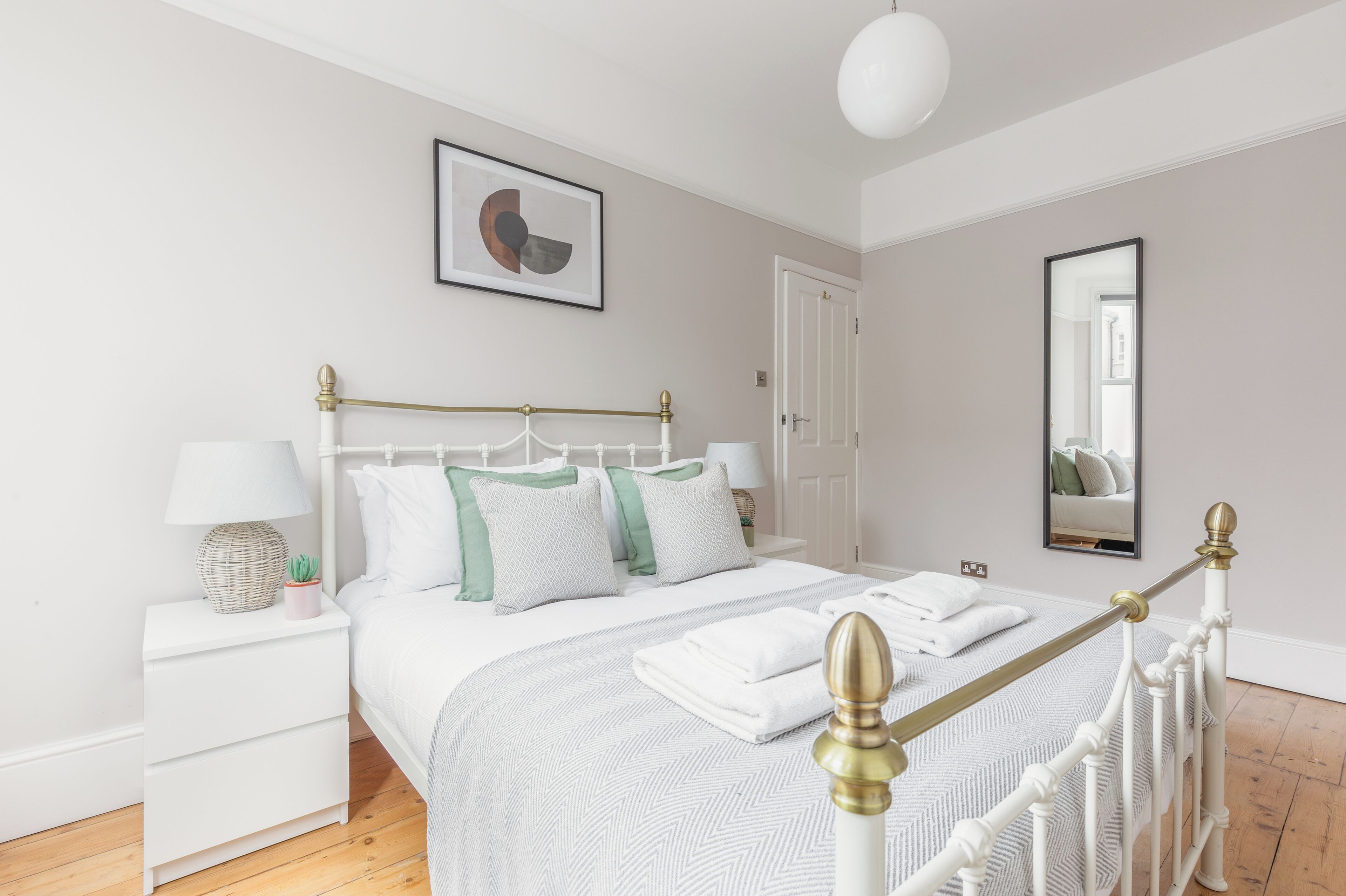 Une chambre à coucher bien rangée, avec un lit, des tables de chevet, une lampe et un miroir.