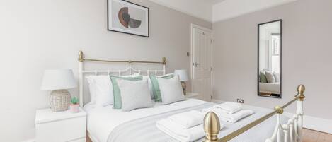 A neatly arranged bedroom with a bed, bedside tables, a lamp, and a mirror.