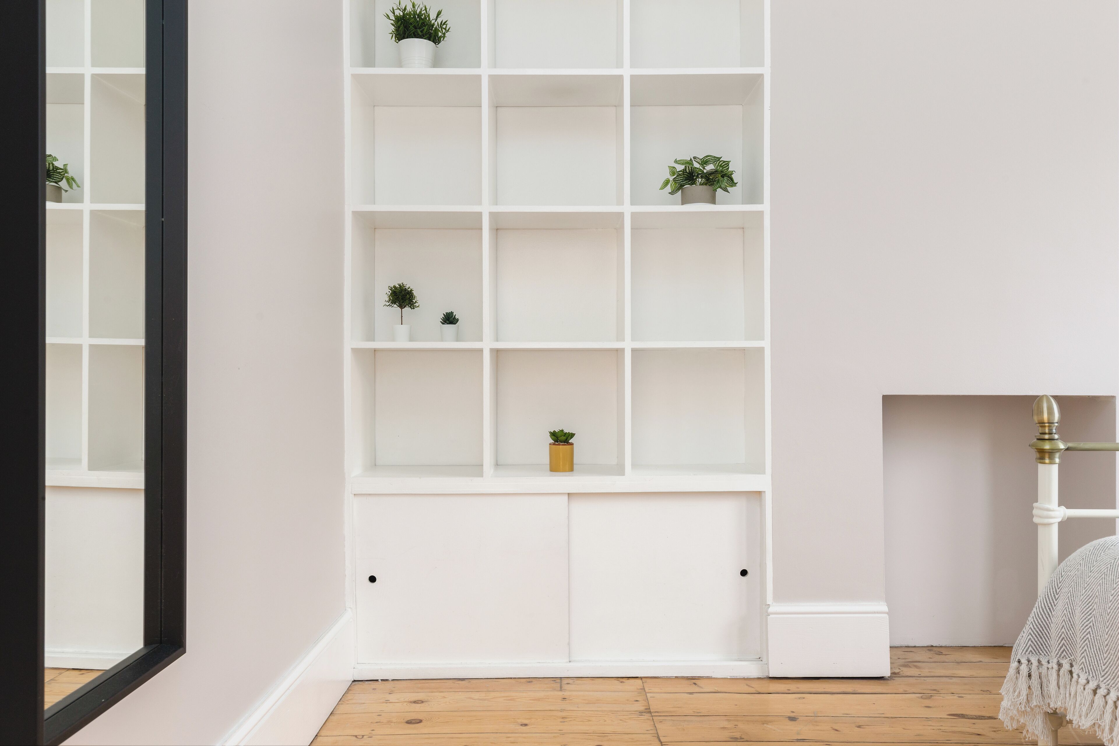 Une bibliothèque encastrée blanche, dotée de plusieurs étagères, dont certaines contiennent de petites plantes en pot.