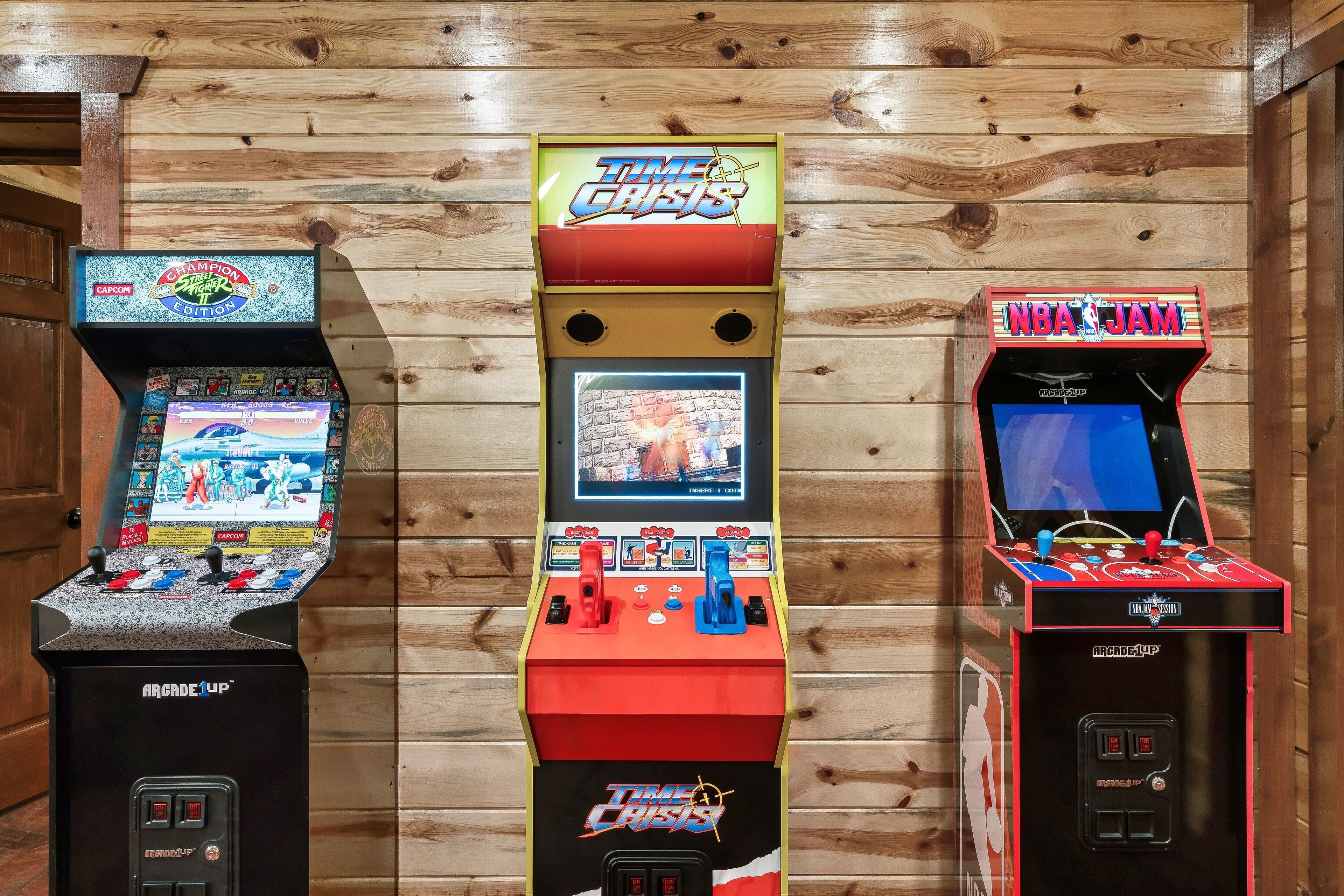 Three arcade machines: Time Crisis, Capcom, and NBA Jam, against a wooden wall.