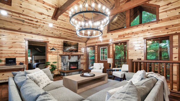 A log cabin interior with a fireplace, wooden walls, a large sofa, and a chandelier. - Big Chief Lodge (Sevierville)