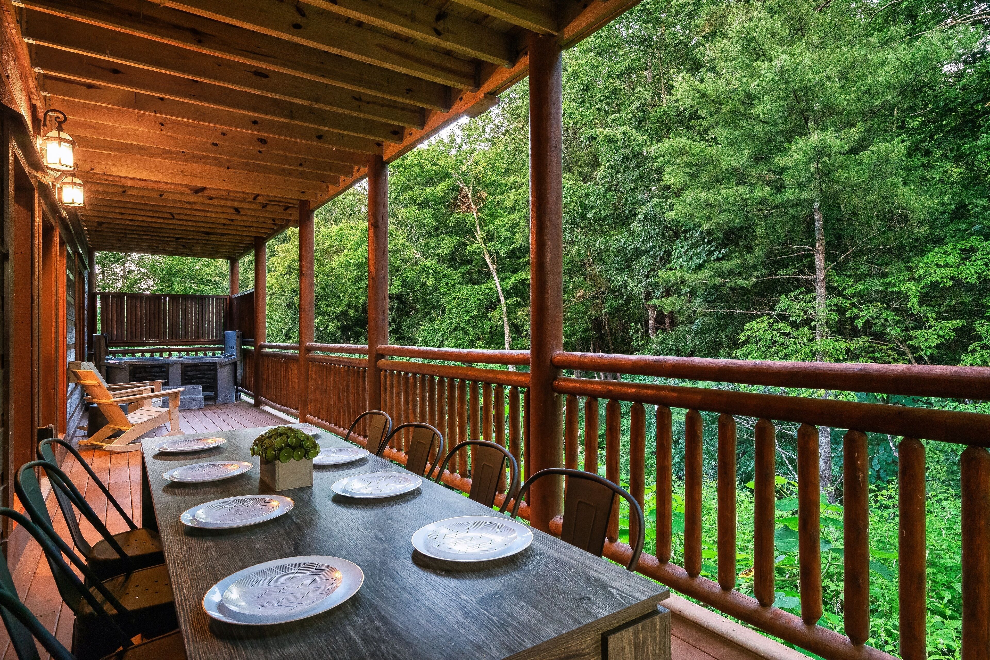 A wooden deck with a table set for dining, surrounded by chairs, and overlooking a forested area.