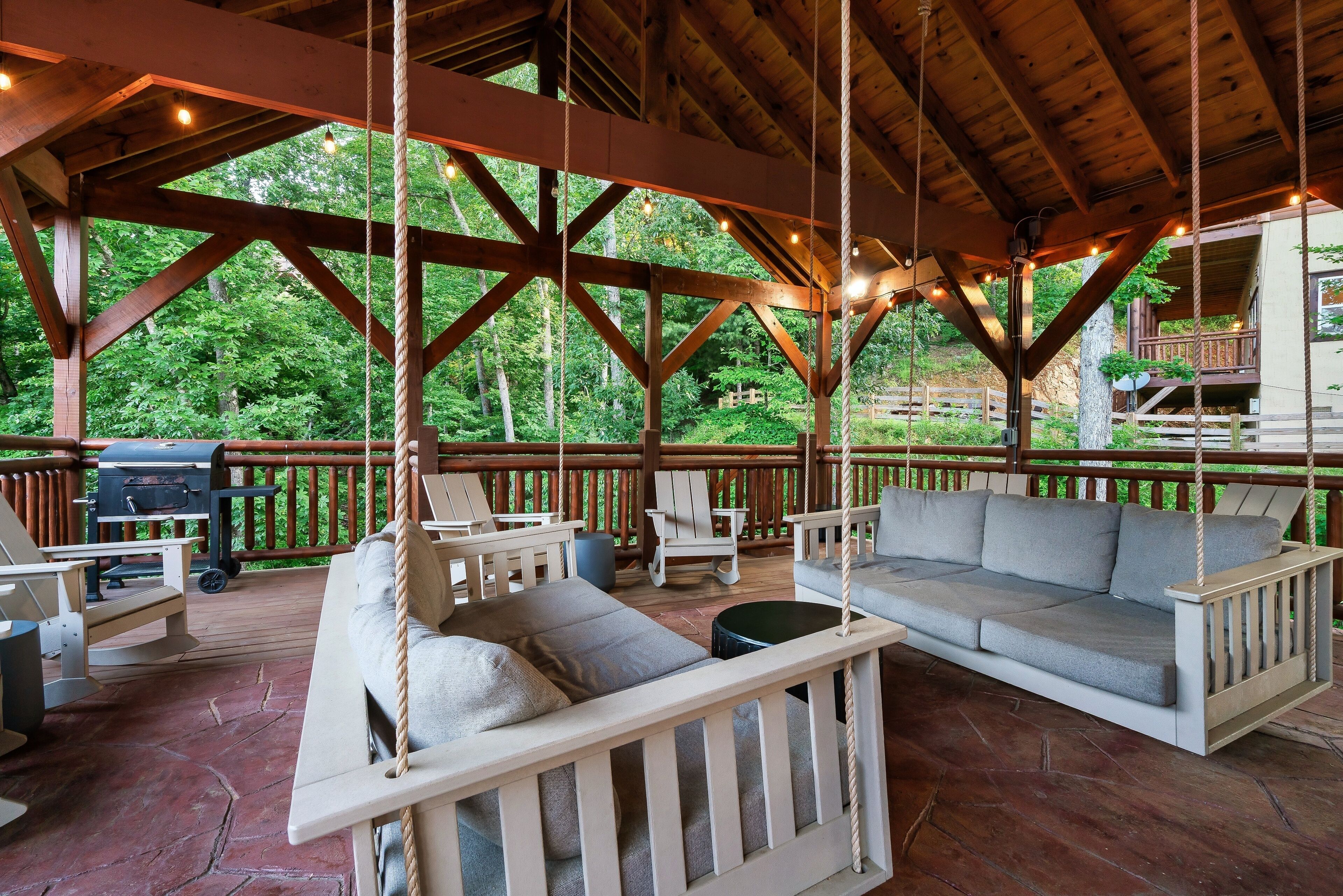 A covered outdoor seating area with a swing, a sofa, and a grill.
