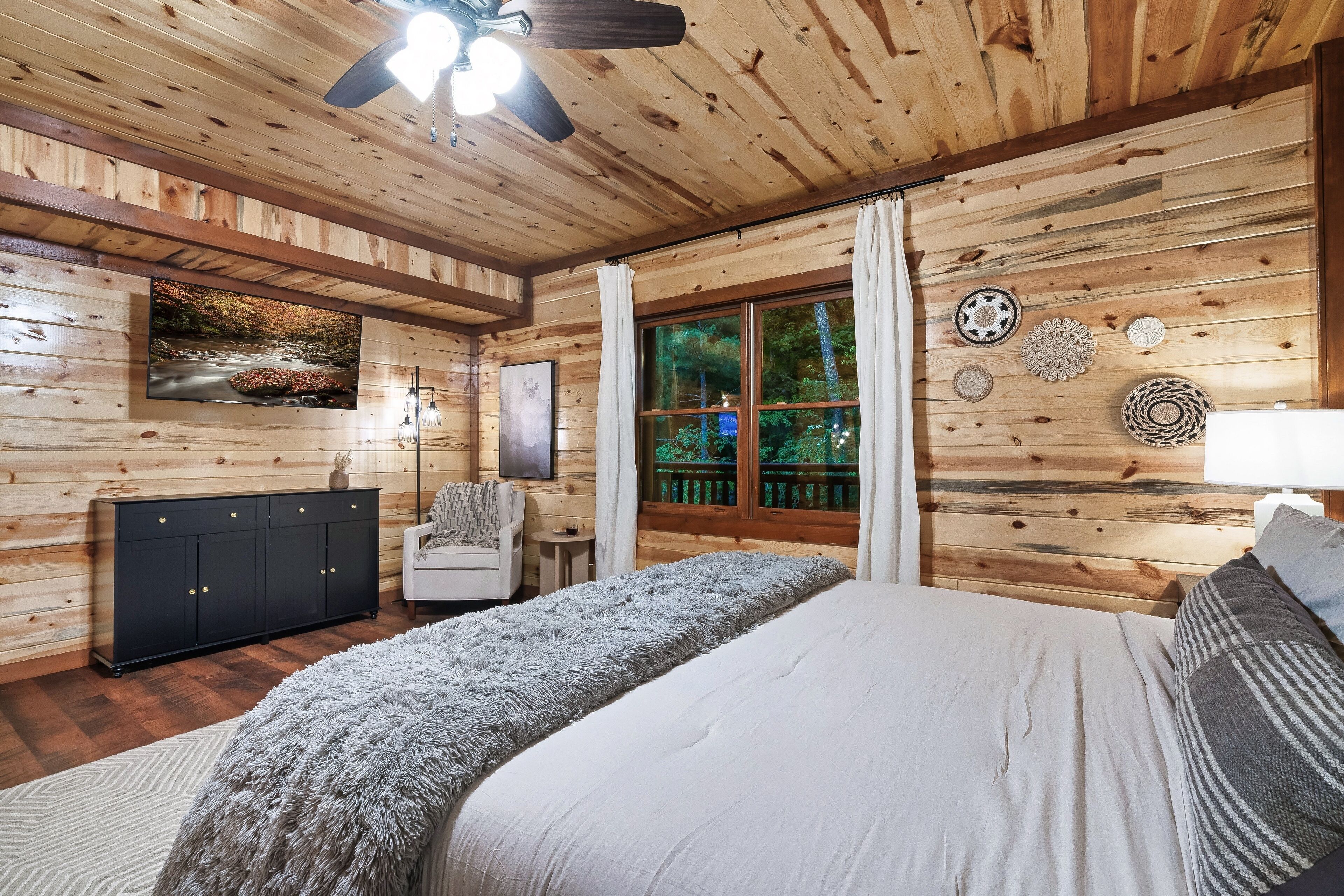 A wooden cabin bedroom with a bed, a dresser, a chair, and a window with curtains.