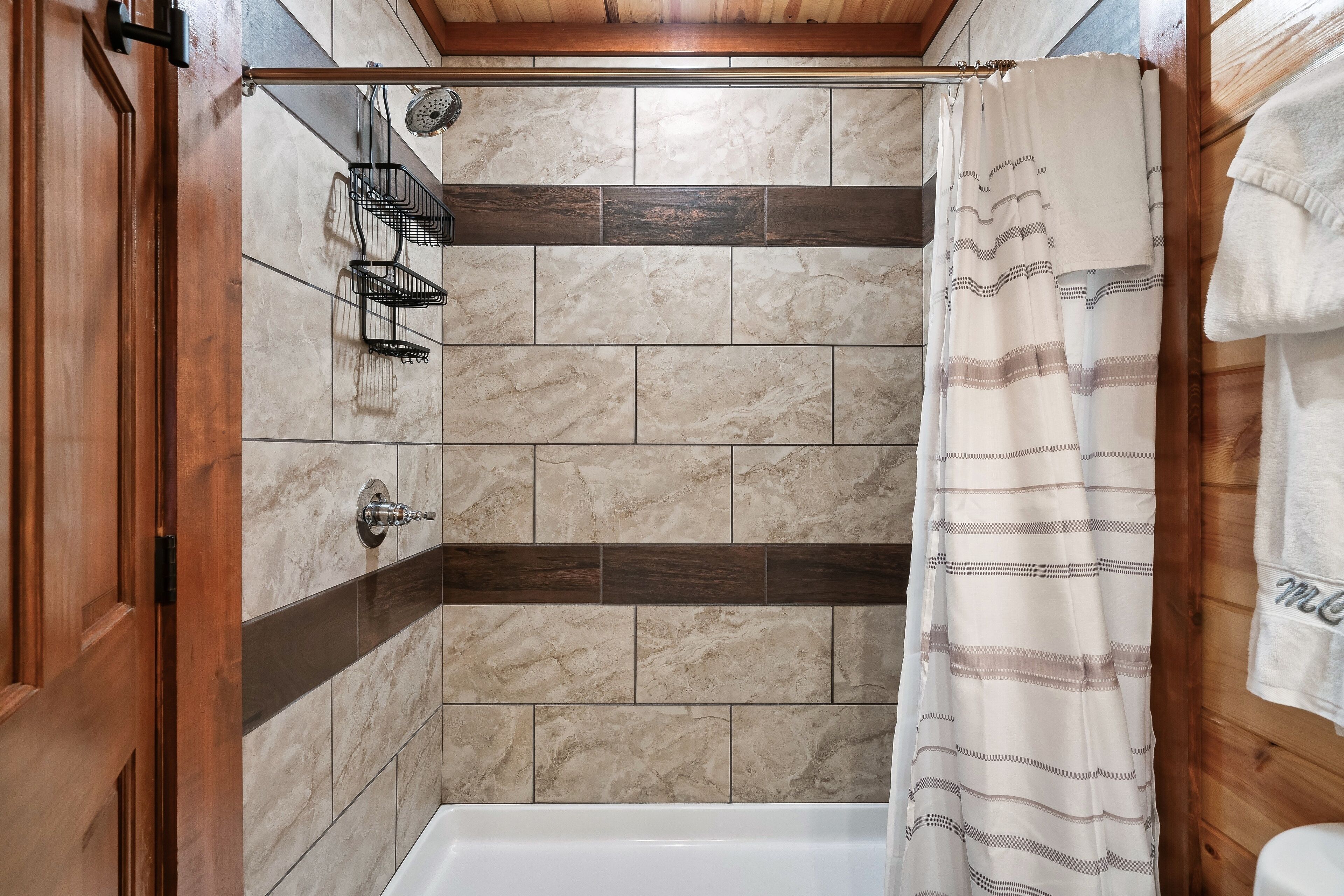 A shower area with a wooden door, a towel rack, and a shower curtain.
