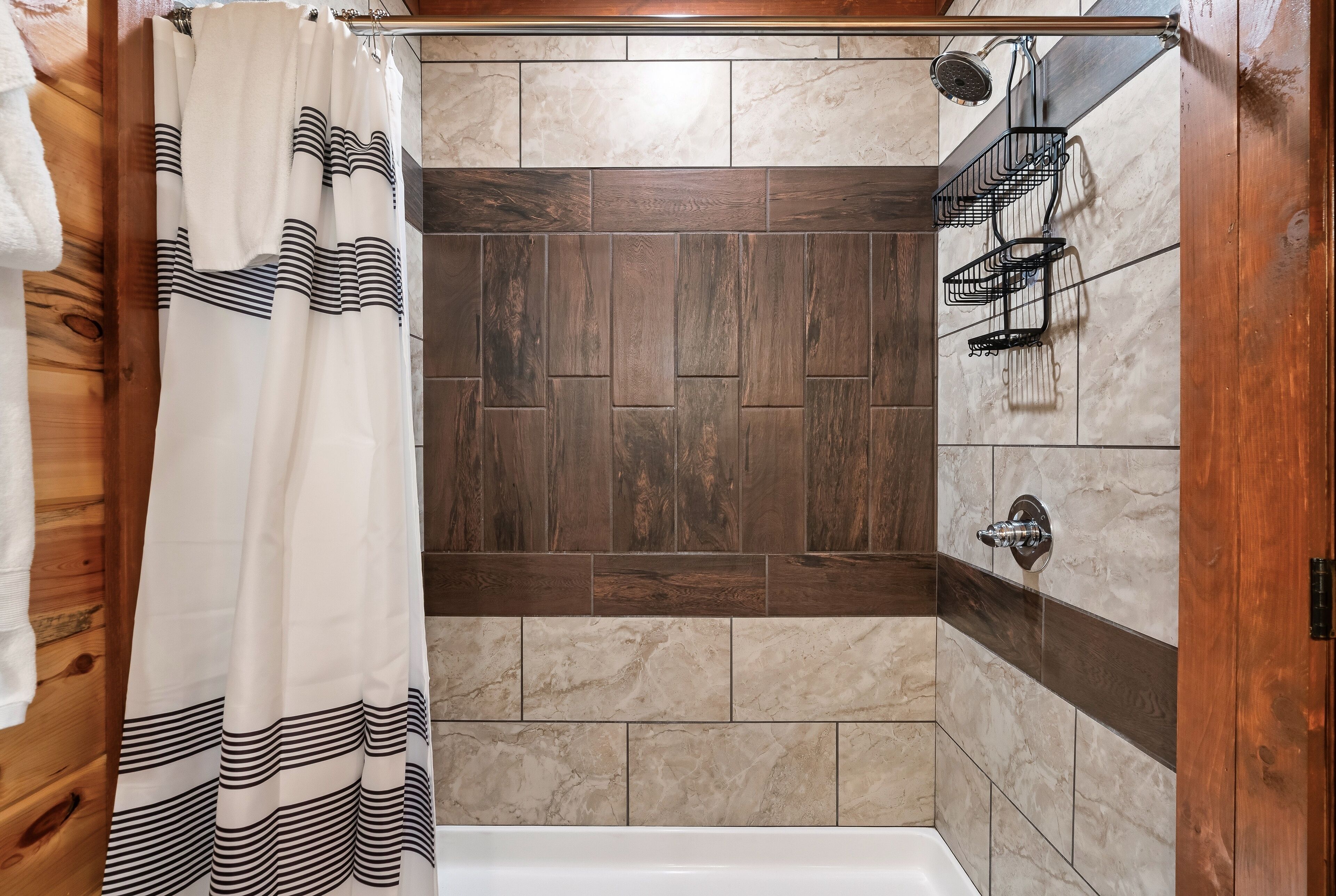 A shower area with a wooden door, a shower curtain, and a tiled wall with a herringbone pattern.