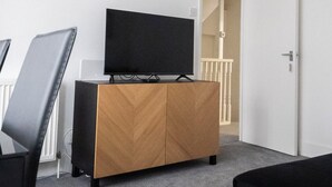 Un soggiorno moderno con una TV a schermo piatto su un mobile in legno, un divano nero e un tappeto grigio.