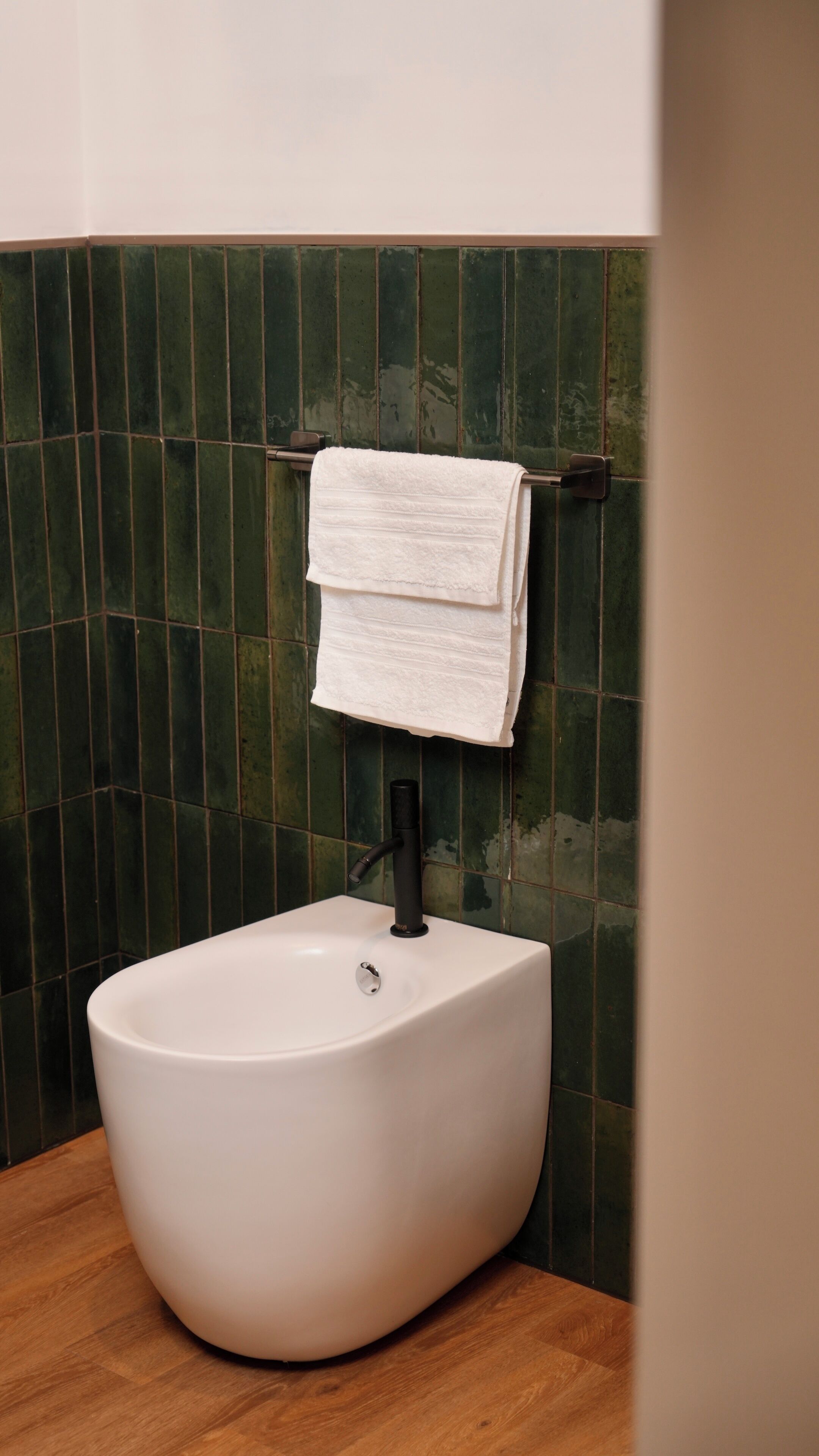 Casa de banho com lavatório pedestal branco, toalha pendurada em suporte e paredes com azulejos verdes.