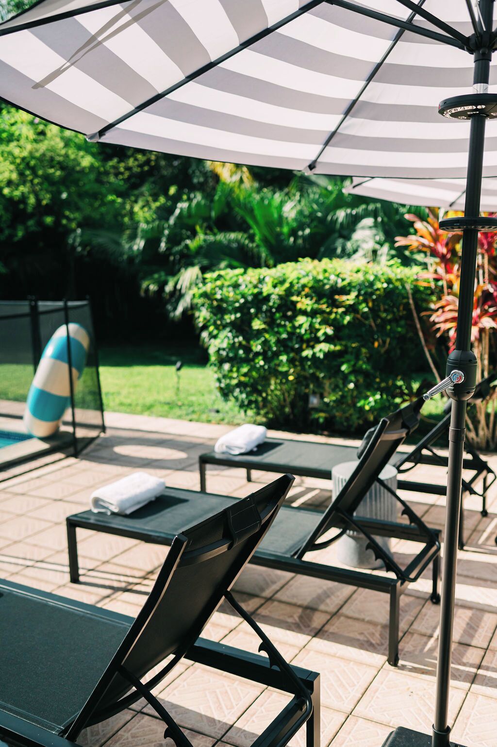 A poolside area with lounge chairs, a striped umbrella, and a pool with a blue and white ball.