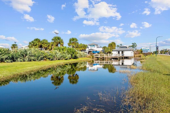 Ein Hotel am Wasserufer mit Reflexionsbecken, Palmen und blauem Himmel.