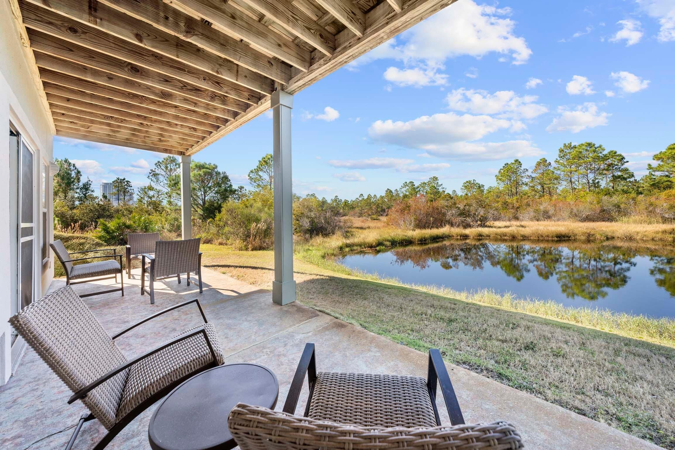 An outdoor patio with wicker furniture and a view of a pond and trees.