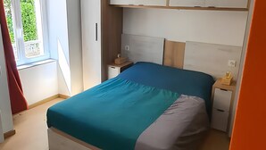 Un dormitorio con cama, mesitas de noche, una ventana y una puerta.