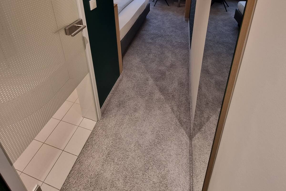 A hotel room with a bed, a desk, a chair, a radiator, and a window with curtains.