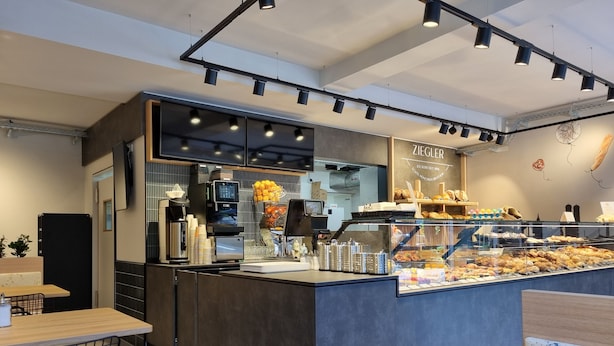 Een modern caféinterieur met een toonbank waarop gebak, een koffieapparaat en een koelvitrine staan.