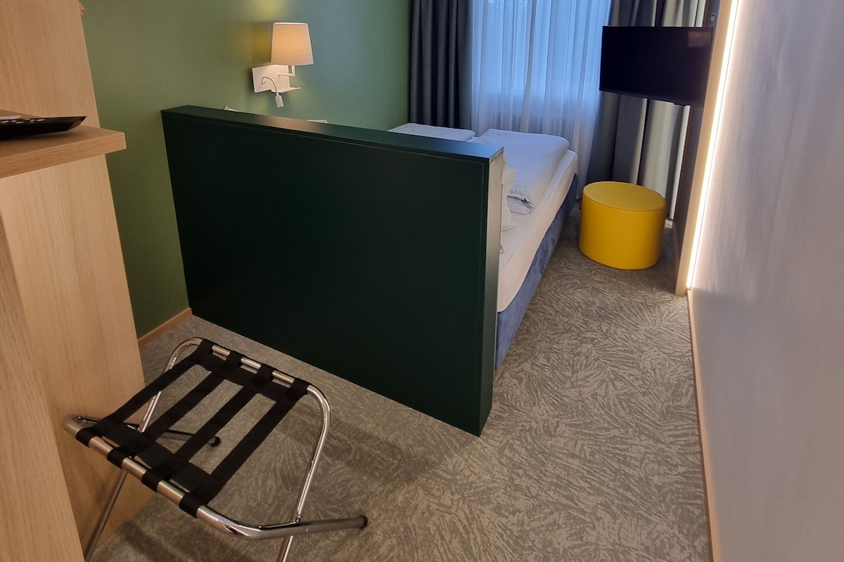 A hotel room with a bed, a desk, a chair, a TV, and a window with curtains.