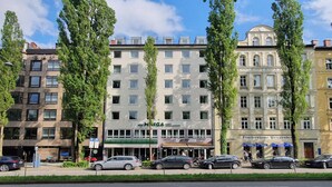 Een hotel met een moderne gevel, meerdere verdiepingen en een groene luifel.