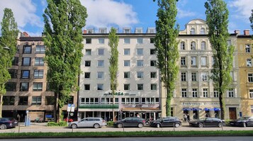 Un hotel con una facciata moderna, diversi piani e un tendone verde.