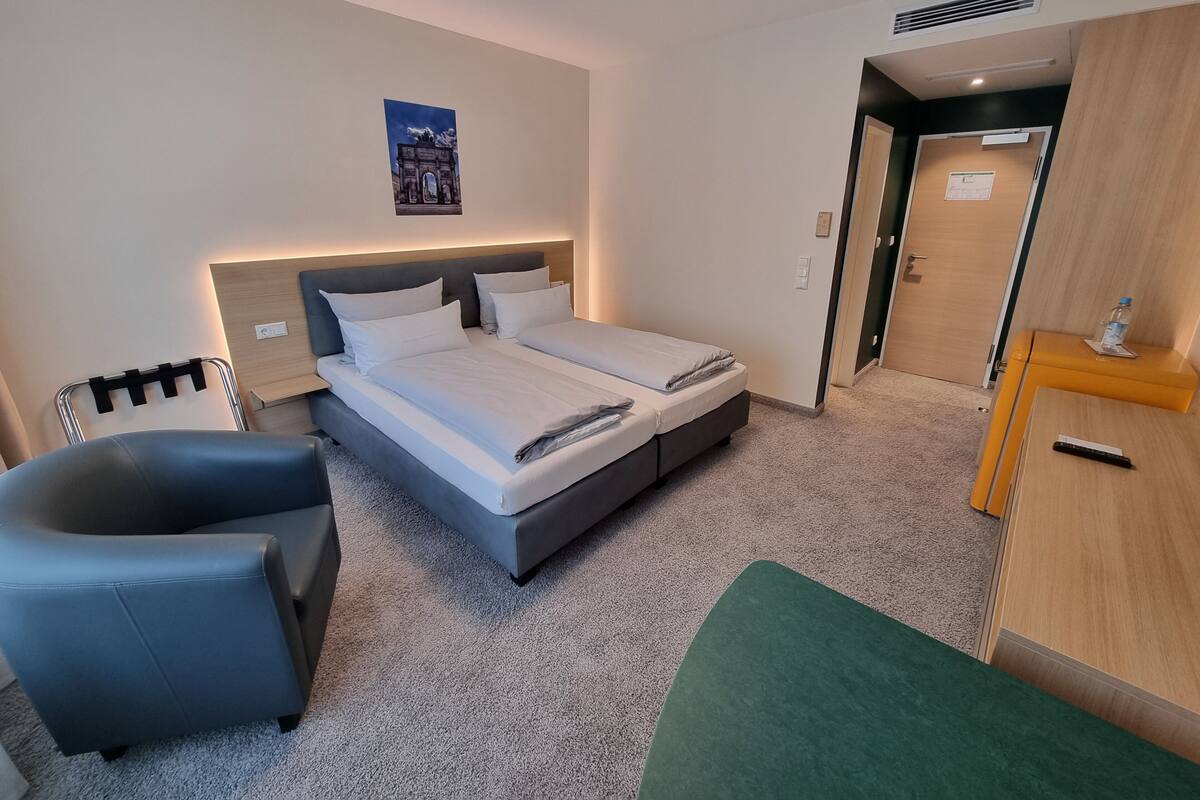 A hotel room with a bed, a chair, a desk, and a door.
