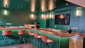 Een bar met een groene wand, barstoelen en een toonbank met glazen en een blender.