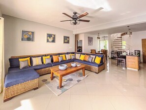 A spacious living area with a large sectional sofa, a wooden coffee table, and a dining area with a spiral staircase. - 3BD apt in central Cabarete, steps from beach (Cabarete)