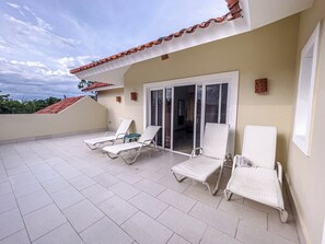 A covered outdoor area with white lounge chairs, a tiled floor, and a building entrance with a glass door. - 3BD apt in central Cabarete, steps from beach (Cabarete)