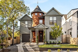A two-story house with a turret, a front porch, and a well-maintained lawn. - The Vic on 10th • Skyline Views • Heated Pool • 2025 Build • Firepit (Austin)