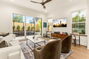 A modern living room with a sofa, armchairs, a coffee table, and a TV mounted on the wall. - The Vic on 10th • Skyline Views • Heated Pool • 2025 Build • Firepit (Austin)