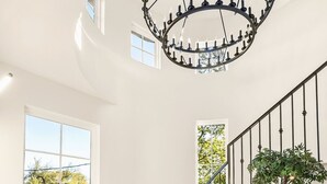 Ein modernes Interieur mit einer Holztreppe, einem Chandelier und einem Essbereich mit Tisch und Stühlen.