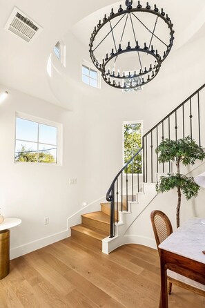A modern interior with a wooden staircase, a chandelier, and a dining area with a table and chairs. - The Vic on 10th • Skyline Views • Heated Pool • 2025 Build • Firepit (Austin)