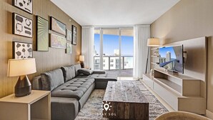 Una habitación de hotel moderna con un sofá grande, una mesa de centro, un televisor de pantalla plana y obras de arte en las paredes.