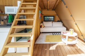 A loft-style room with a wooden staircase, a sofa, a small table, and a window. - Tipi Lodge Glamp 'Marguerite' with Nordic Bath, Private Terrace, and Air Conditioning (Le Boulou)