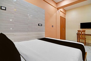A hotel room with a bed, a television, and a wooden chair. - Classic The AX Inn (Kolkata)
