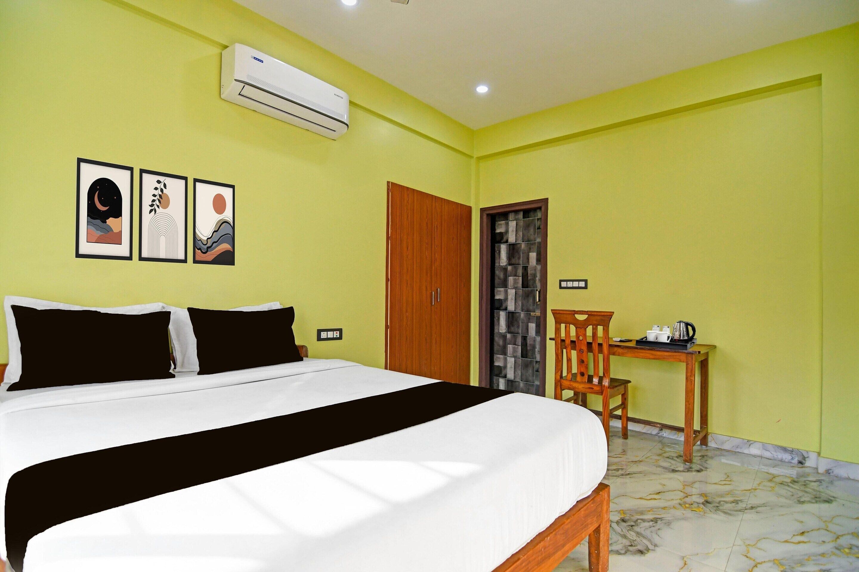 A hotel room with a bed, a wooden chair, a small table, an air conditioning unit, and a door with a glass panel.