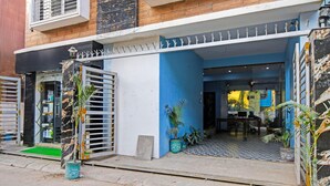 Un edificio con fachada azul, entrada protegida por una reja y plantas en macetas.
