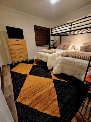 Ein Schlafzimmer mit zwei Betten, einem Fernseher, einer Holzkommode und einem Teppich mit Muster.