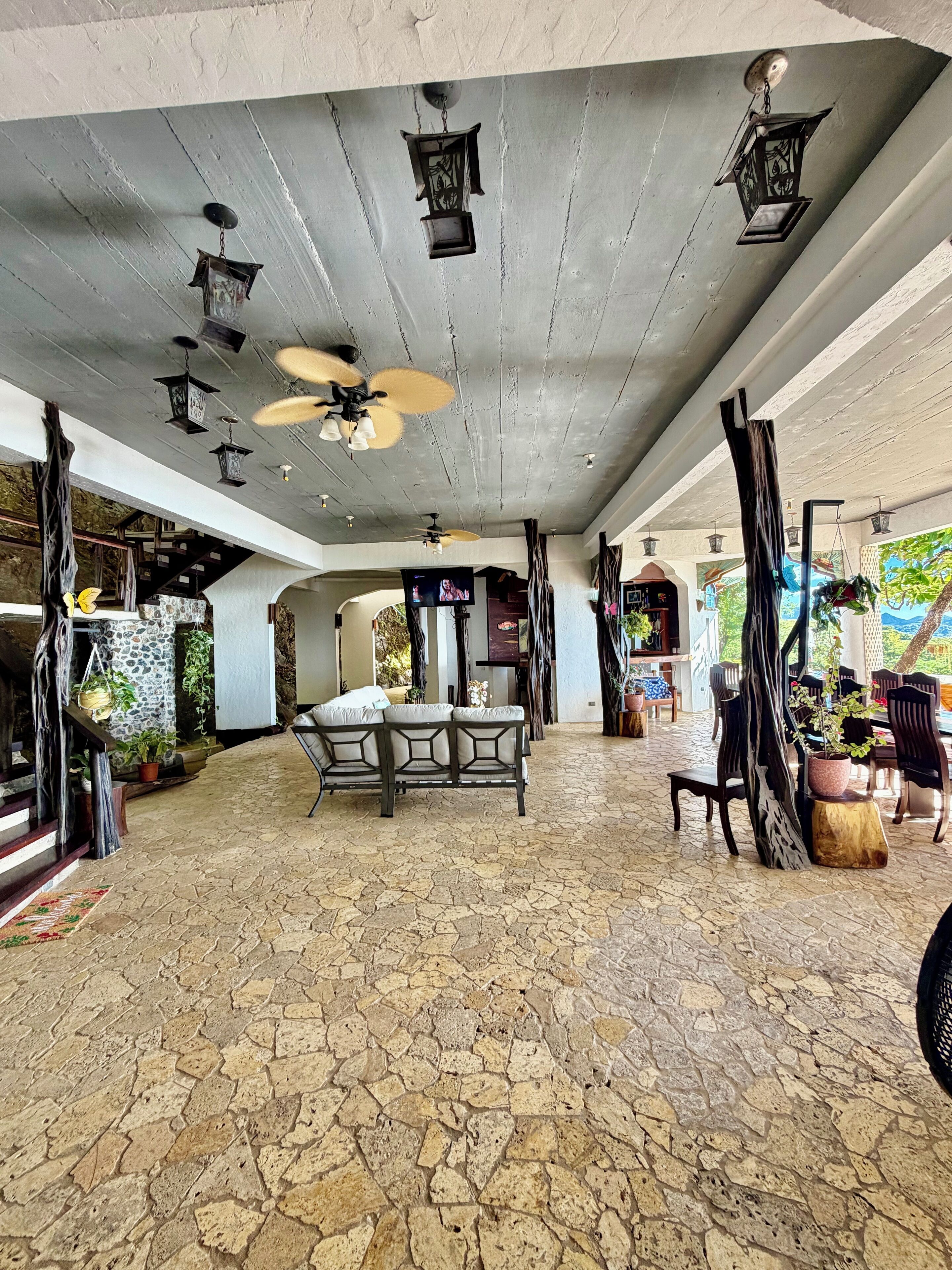 A spacious outdoor area with a stone floor, a ceiling fan, and multiple hanging lanterns.