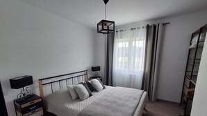 Ett välordnat sovrum med en säng, sängbord, en lampa och ett fönster med gardiner.