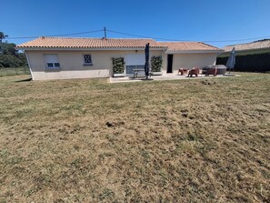 Einbungalow mit gefliester Dach und einer überdachten Terrasse mit Gartenmöbeln, umgeben von einem Rasen.