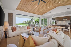 Ein modernes Wohnzimmer mit einer Couch, Sesseln, einem Couchtisch und einem großen Fenster mit Blick ins Freie.