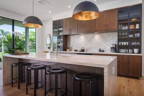 A modern kitchen with a large island, bar stools, wooden cabinets, and pendant lighting. - Hapuna Estates 10 Four Bedroom (Kamuela)