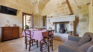 A stone-walled room with a fireplace, a dining table set with a red and white checkered tablecloth, and a sofa. - Villa Saracino by Perle di Puglia (Supersano)