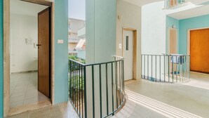 Um corredor com porta de madeira, guarda-corpo de metal e vista para um edifício lá fora.